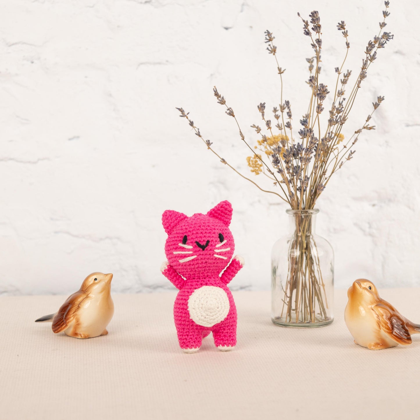a crocheted cat and two small birds next to a vase with flowers