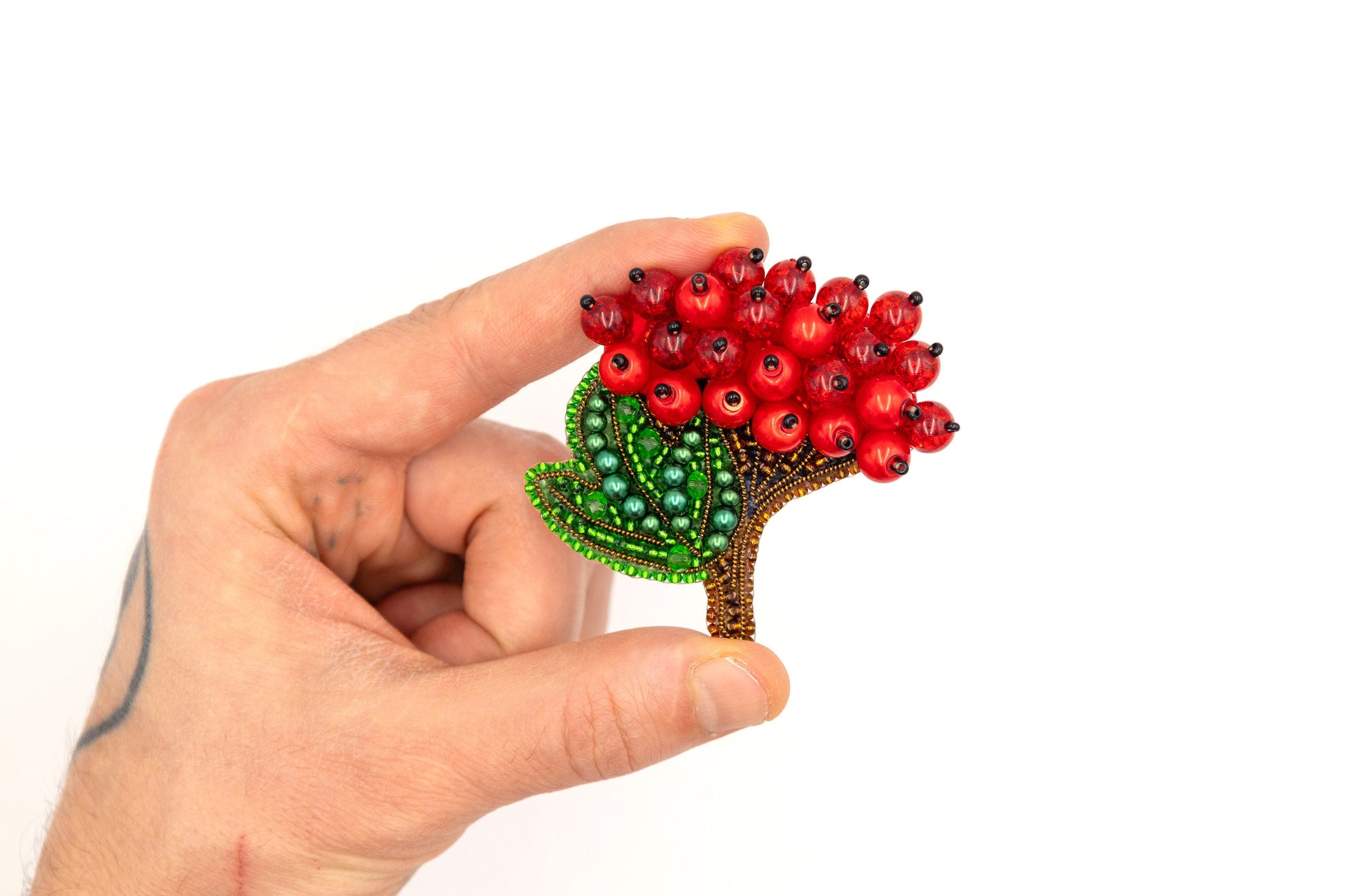 a hand holding a red flower with green leaves