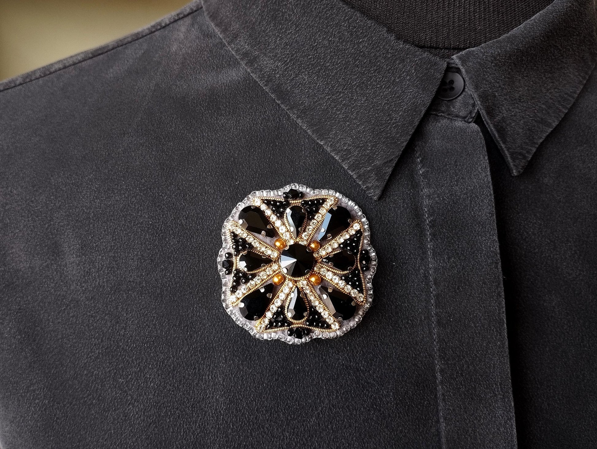 A close-up view of a decorative brooch on a gray shirt collar.