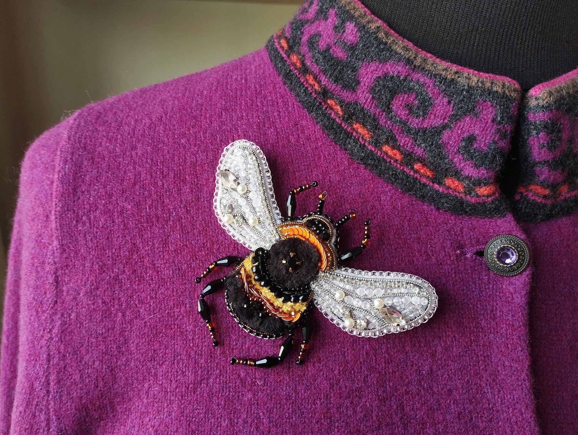 A close-up of a purple sweater with a decorative beaded bee pin on the front.