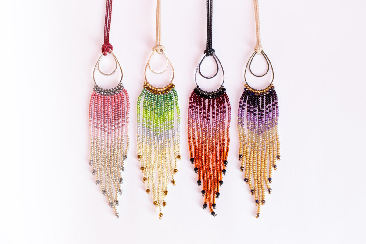 Four colorful beaded earrings with tassels hanging from the ends of strings, arranged in a row.