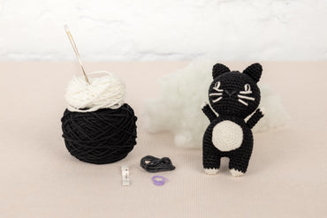 a crocheted cat next to a ball of yarn
