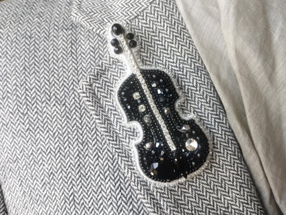 A close-up image of a black and white chevron patterned fabric with a decorative black and silver embellishment resembling a musical instrument, such as a violin or cello.