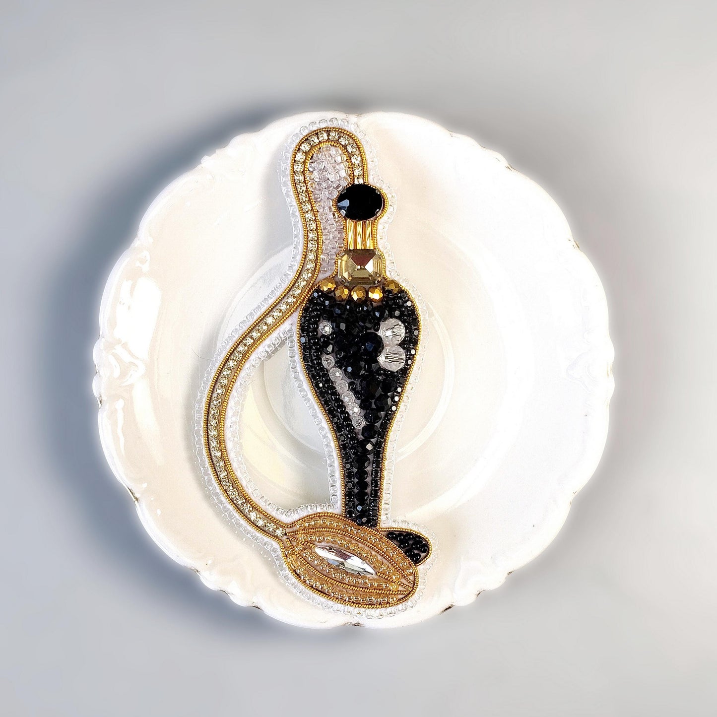A decorative black and gold perfume bottle with a gold cap and a gold chain is displayed on a white plate against a light background.