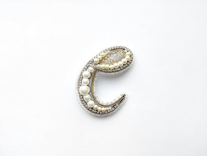 A decorative letter 'C' made of various materials, including pearls, beads, and crystals, against a white background.