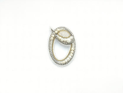 A decorative piece of jewelry, possibly a brooch or pendant, is shown against a white background.