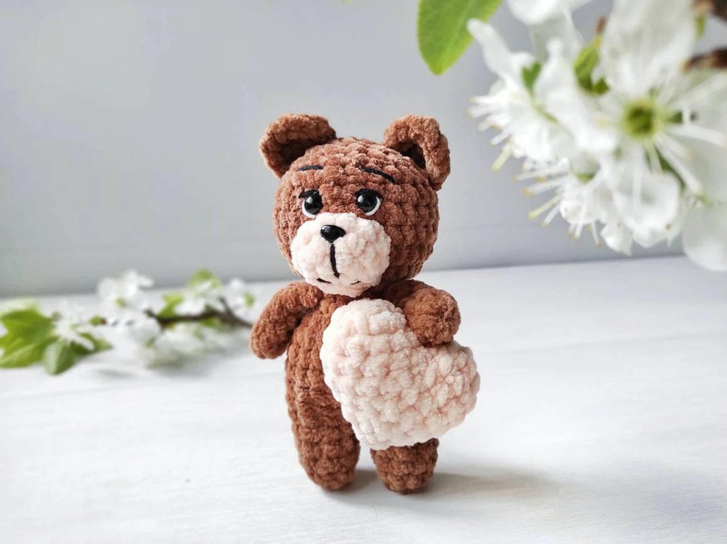 a crocheted teddy bear holding a heart