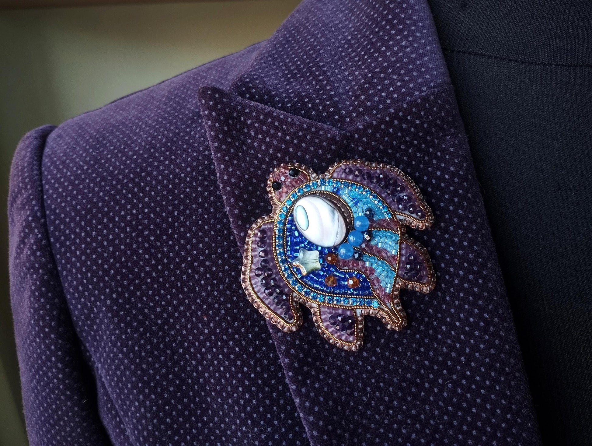 A close-up view of a purple jacket with a decorative brooch featuring a turtle design and various colorful gemstones.