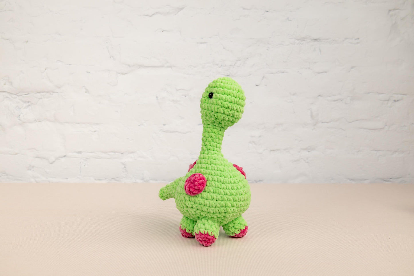 a crocheted green toy with a pink flower on it