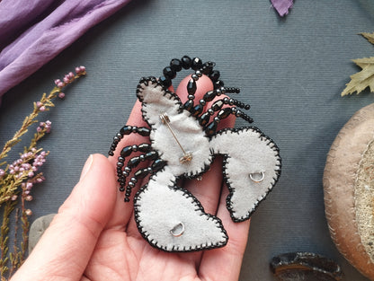 A hand holding a unique, hand-stitched black and white lobster brooch against a gray background.
