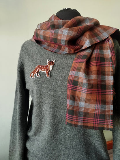 A gray sweater with a patch of a cat embroidered on it, and a plaid scarf draped over the sweater.