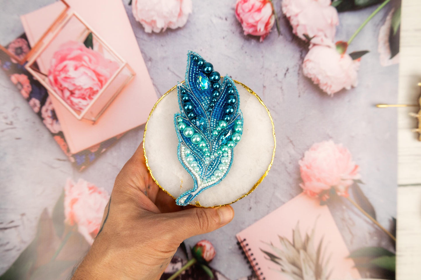 a hand holding a cupcake decorated with a blue feather