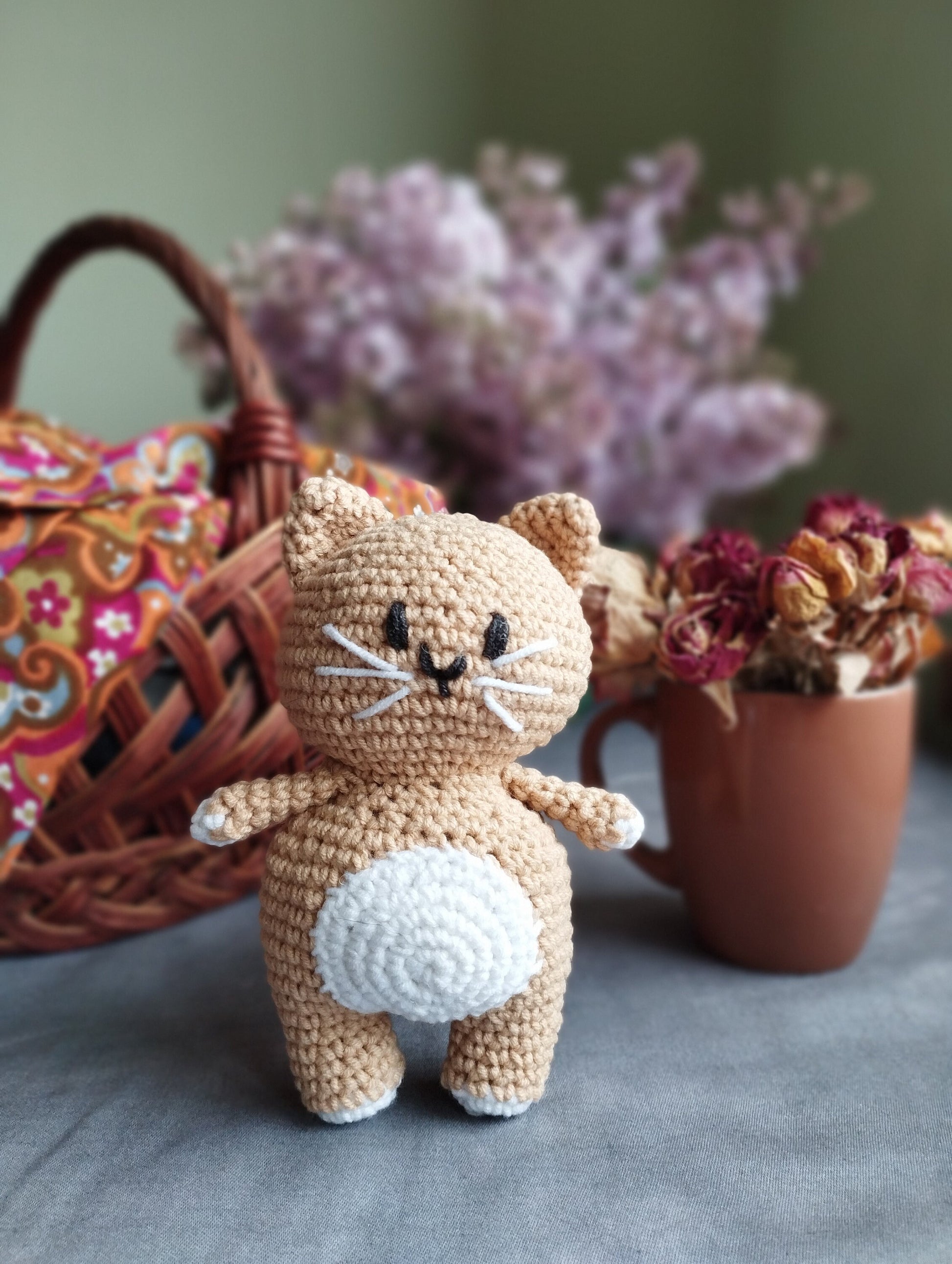 a crocheted cat sitting next to a potted plant
