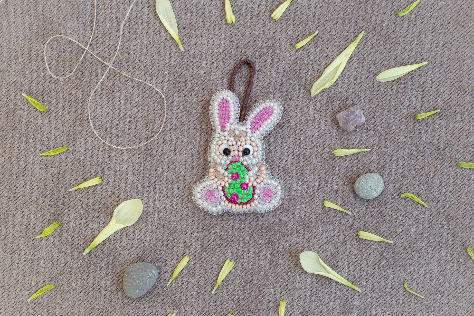 a decorative Easter bunny pendant surrounded by various natural elements, including flower petals, leaves, and small rocks.