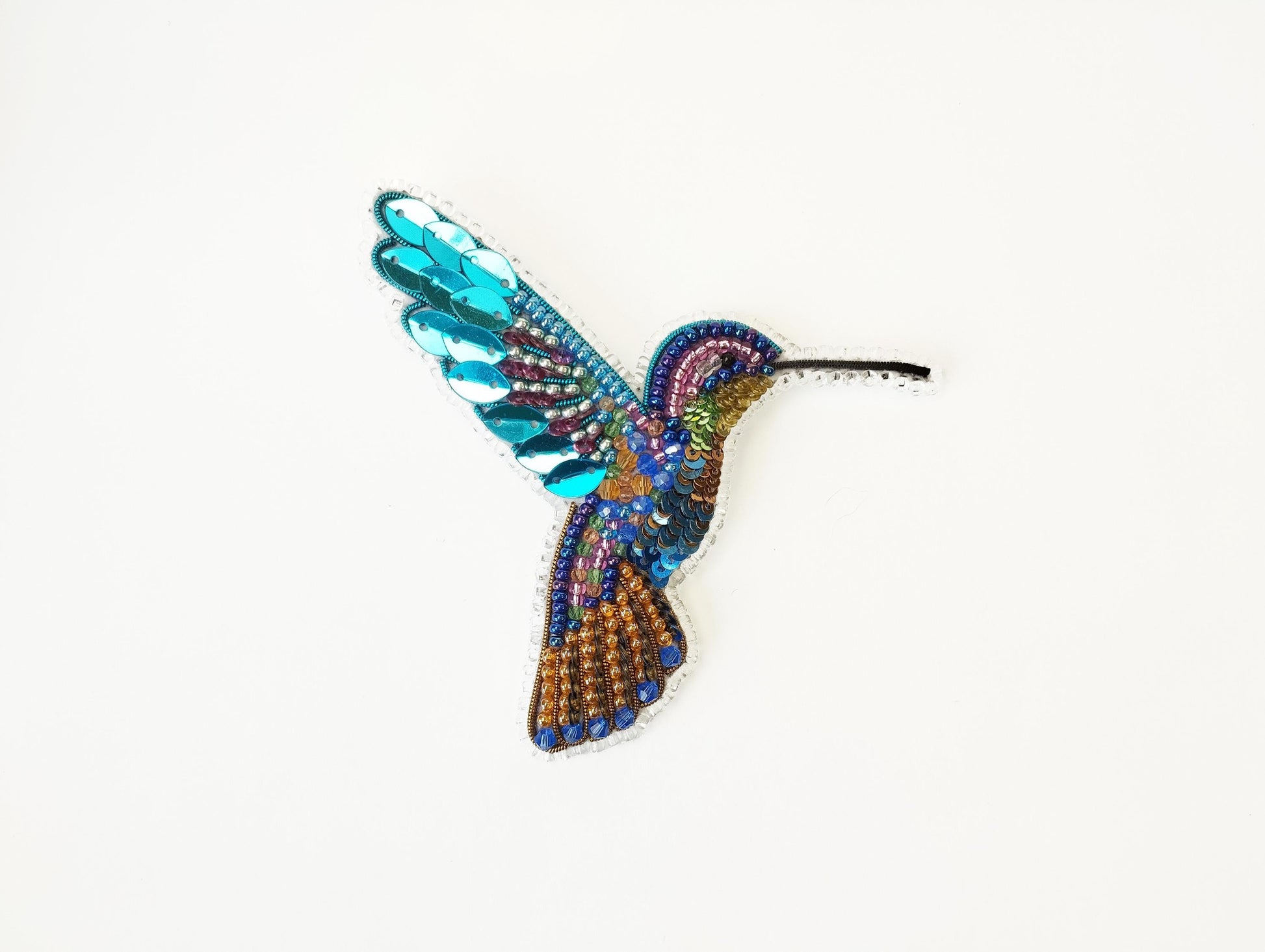 a beaded hummingbird brooch sitting on a white surface