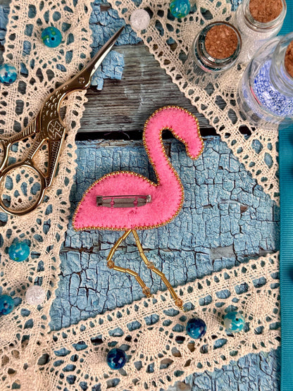 a pink flamingo is sitting on a doily next to a pair of scissors