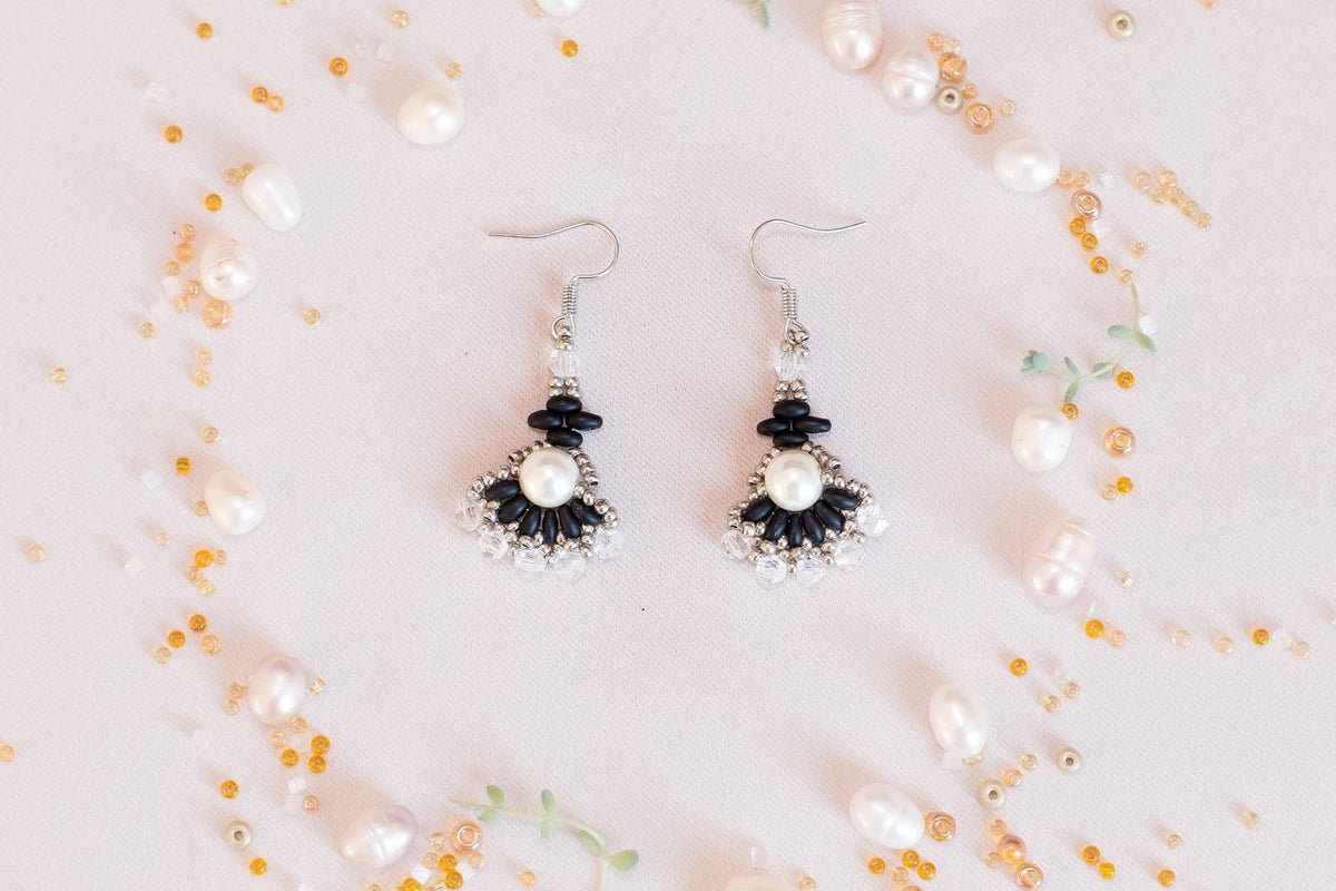 a pair of earrings with black and white accents, surrounded by scattered pearls and beads in various colors.