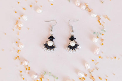 a pair of earrings with black and white accents, surrounded by scattered pearls and beads in various colors.