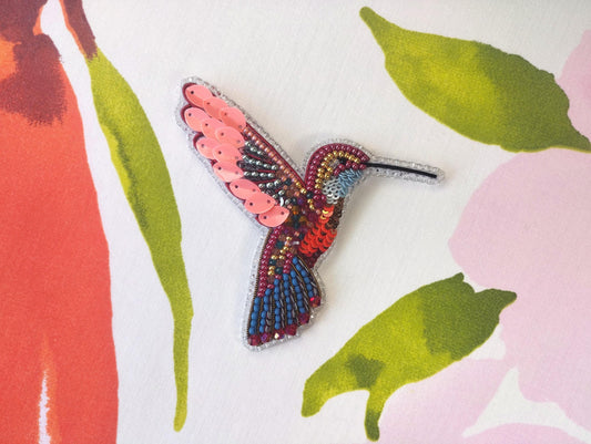 a colorful hummingbird brooch sits on a floral background