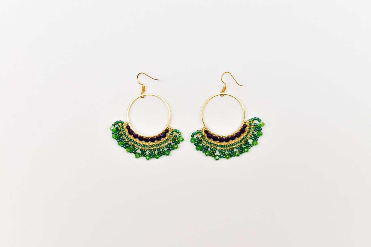A pair of gold hoop earrings with green and purple beads hanging from the bottom.