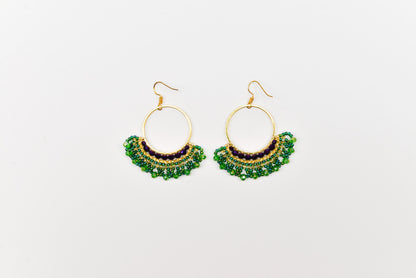 A pair of gold hoop earrings with green and purple beads hanging from the bottom.