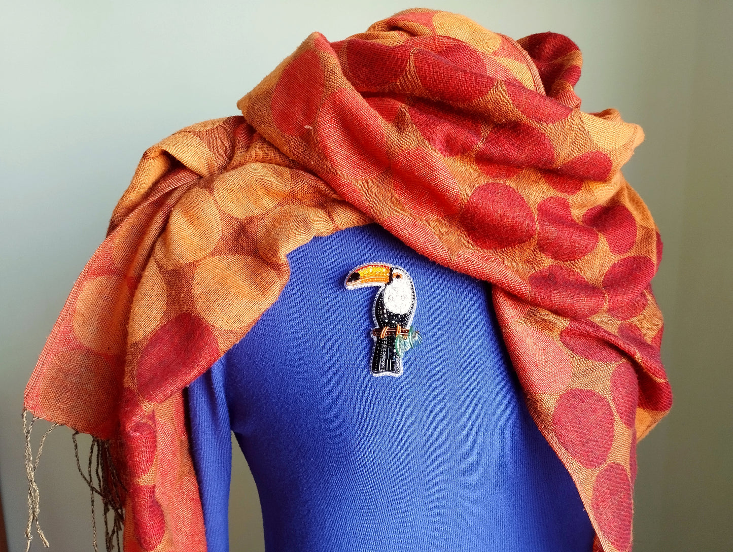 A colorful scarf is draped over a blue sweater, with a small bird brooch pinned to the sweater.