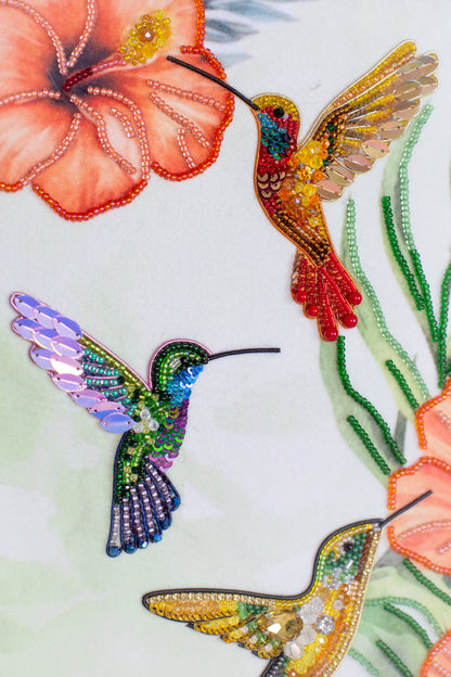 three colorful hummingbirds, each with distinct colors and patterns, against a light green background.