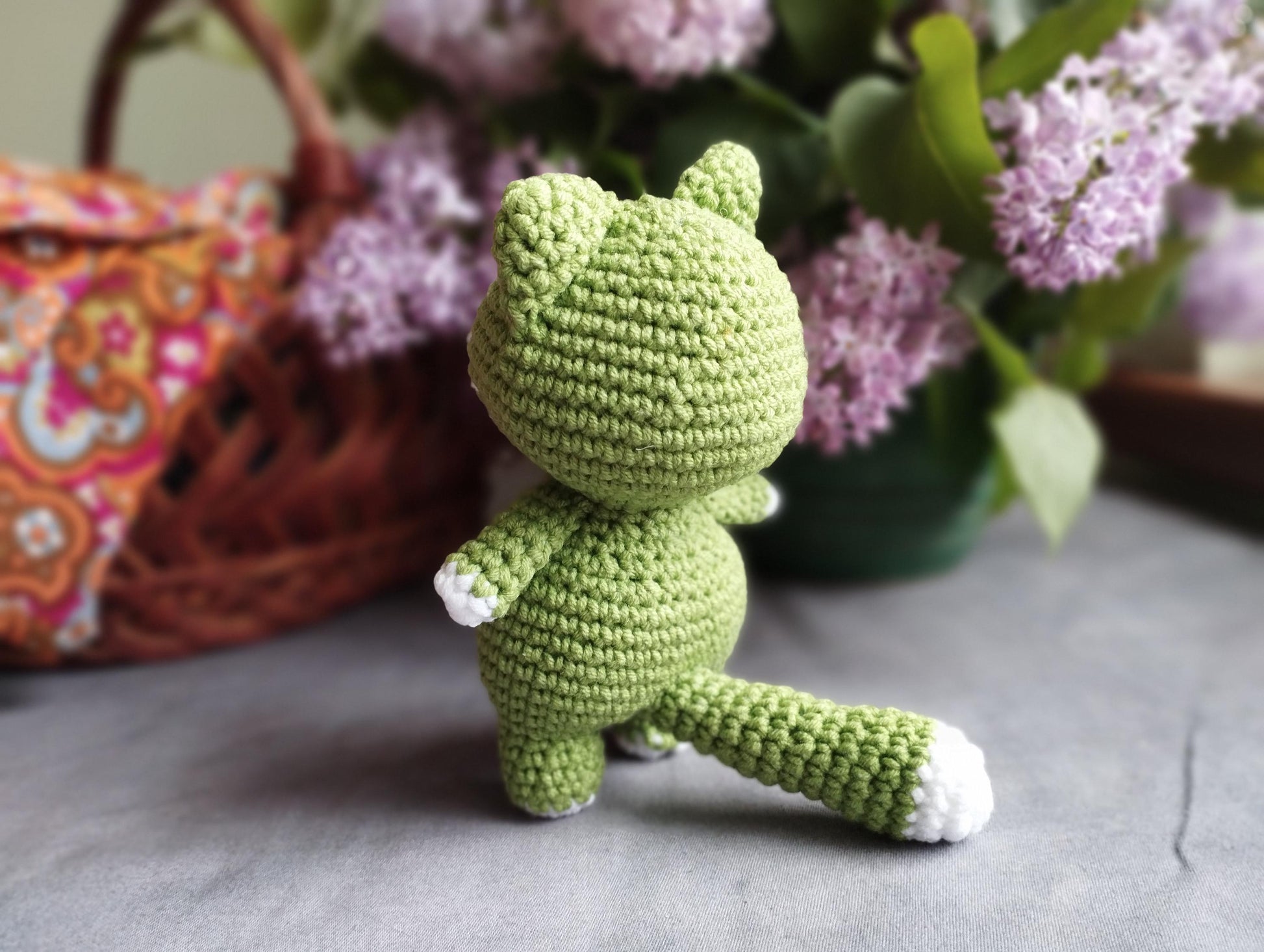 a crocheted green teddy bear sitting next to a basket of flowers