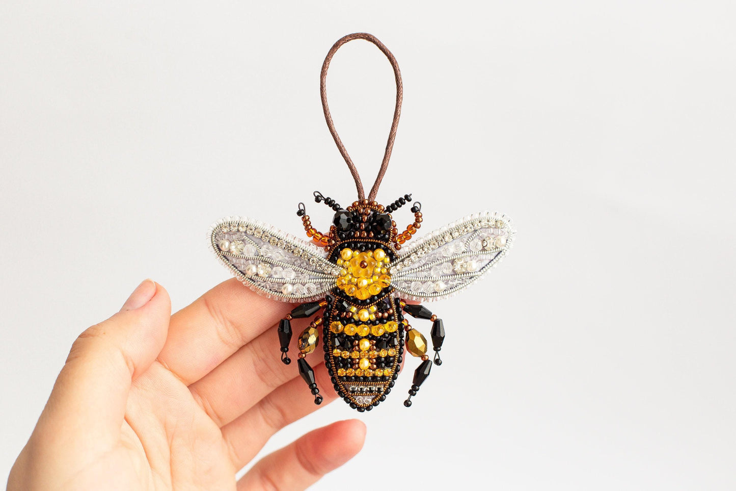 a hand holding a beaded bee ornament