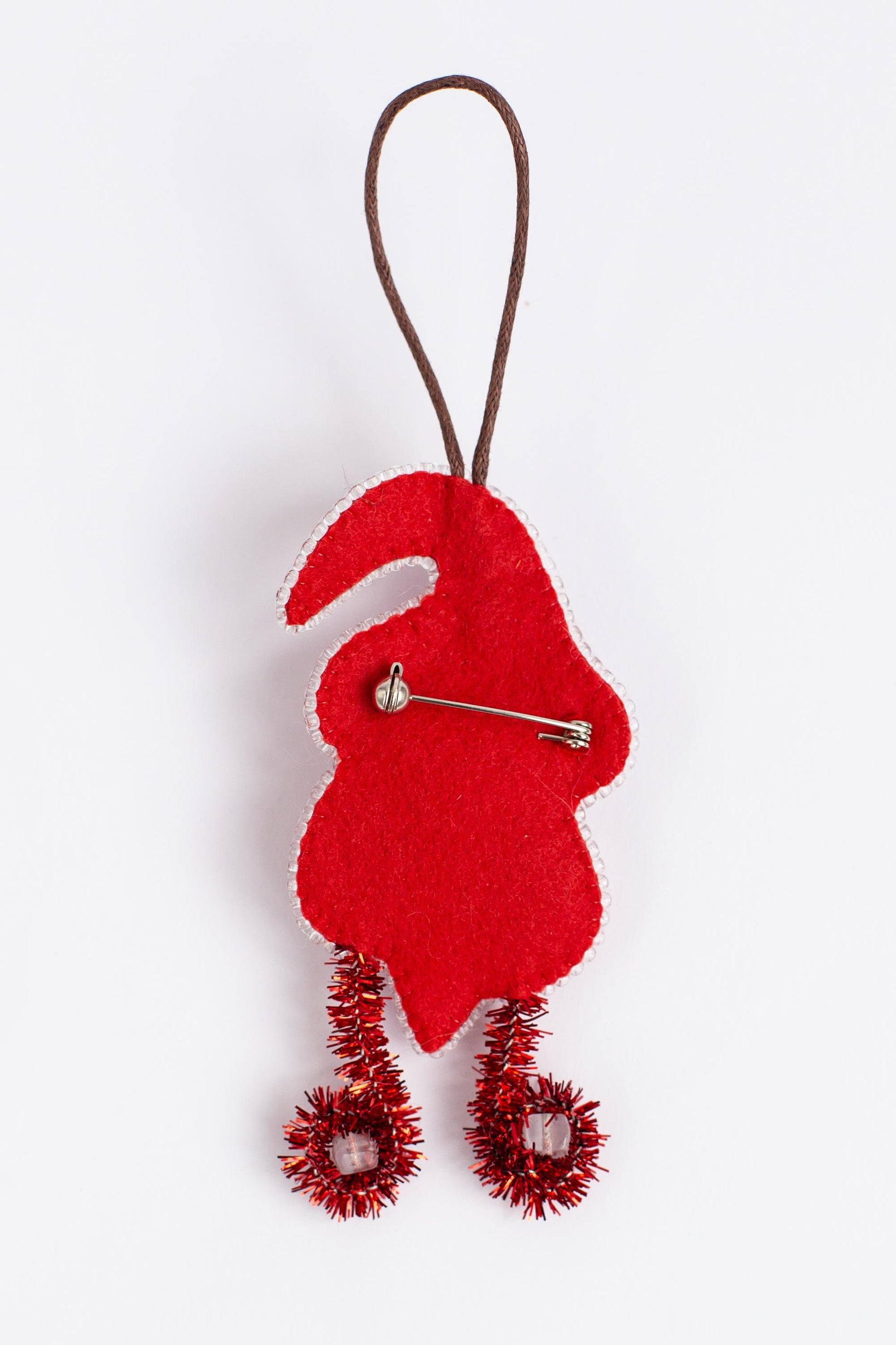 A red felt gnome ornament with a brown cord and red tinsel decorations.