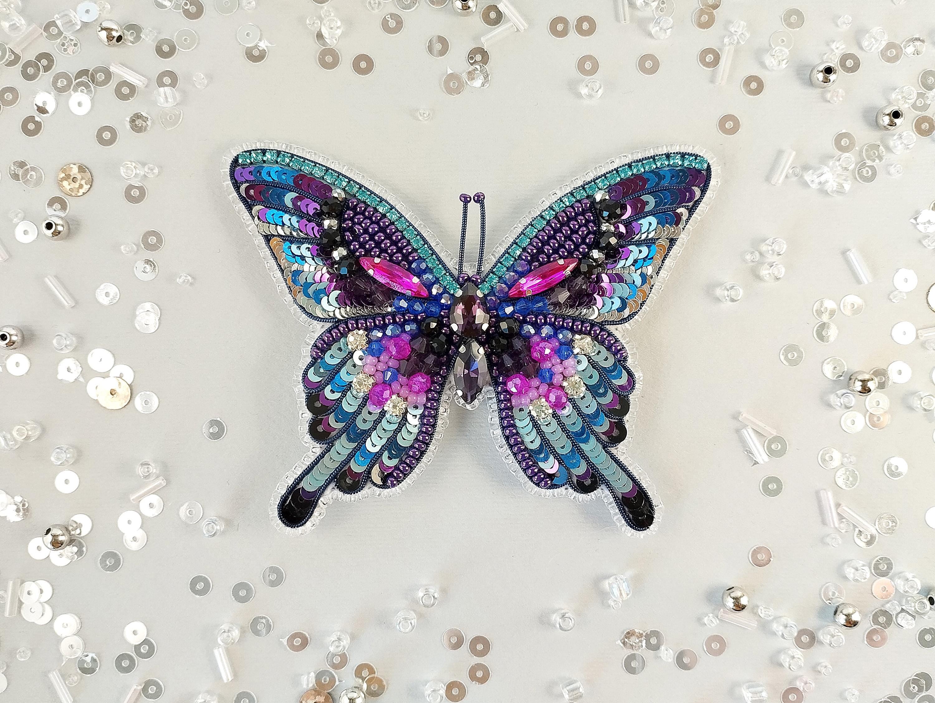 A colorful, sequined butterfly is the central focus of the image, surrounded by scattered sequin pieces on a light background.