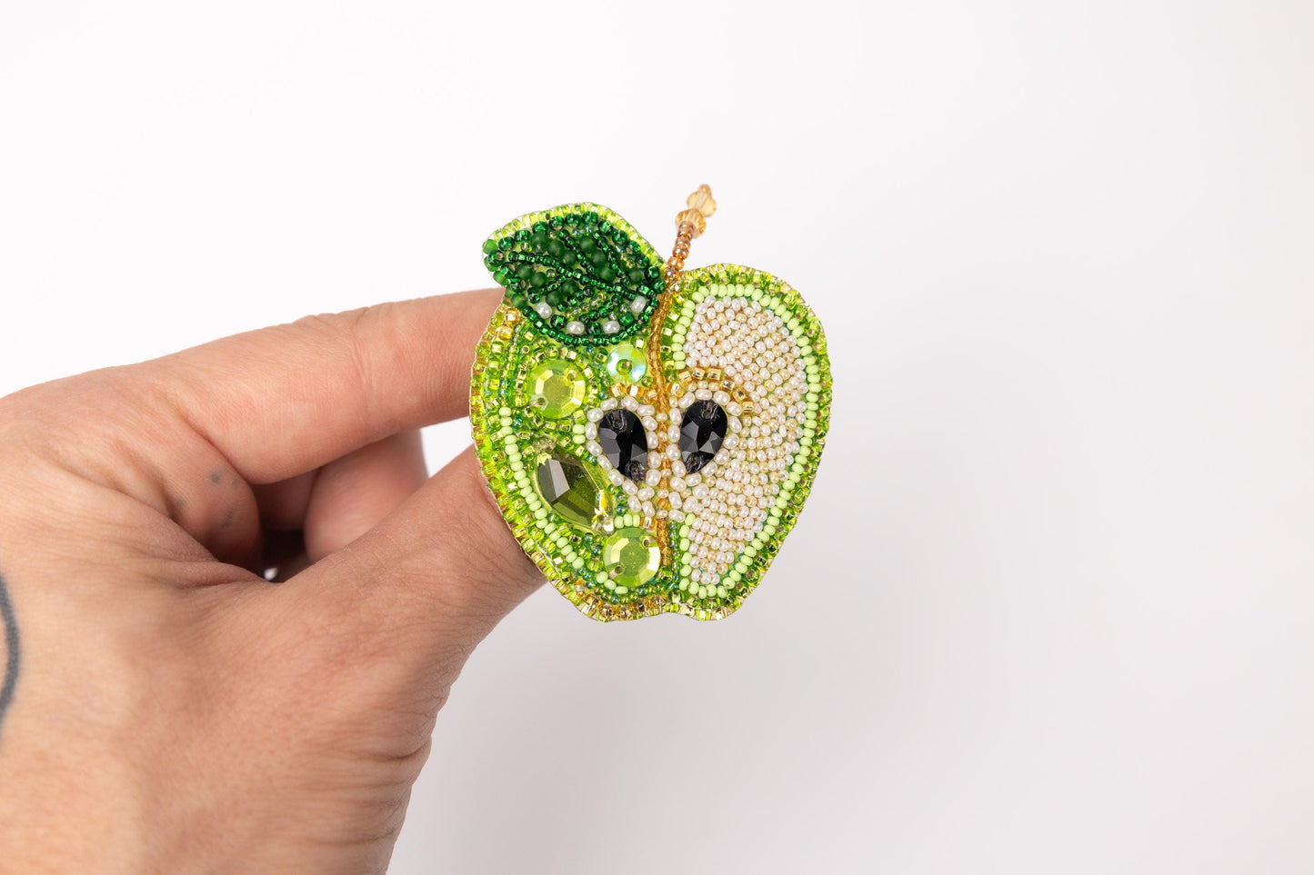 a hand holding a beaded apple brooch