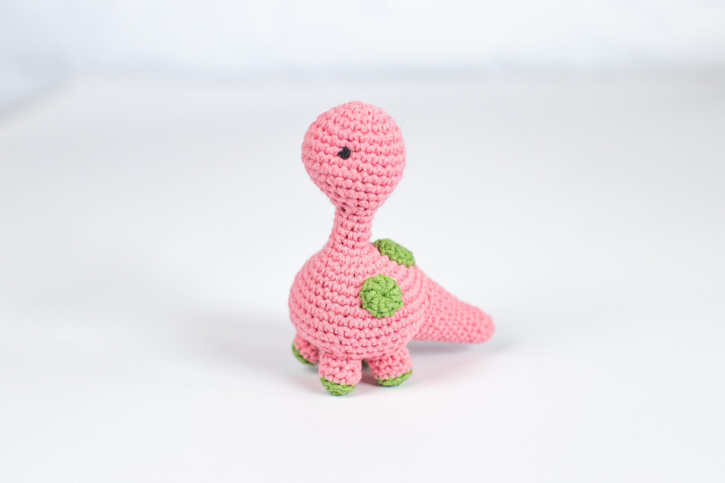 a crocheted pink dinosaur holding a green plant