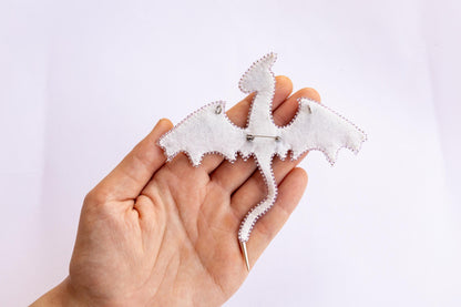 a hand holding a small white brooch with a dragon on it