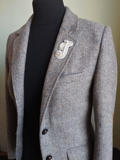 A gray tweed blazer with a white embroidered logo on the left side of the chest.