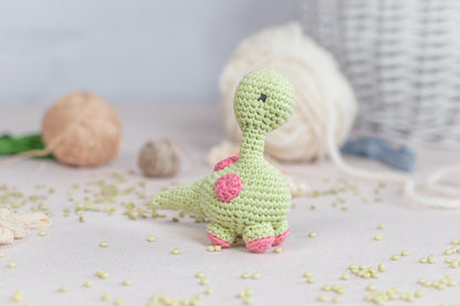 a crocheted toy of a dinosaur next to a ball of yarn