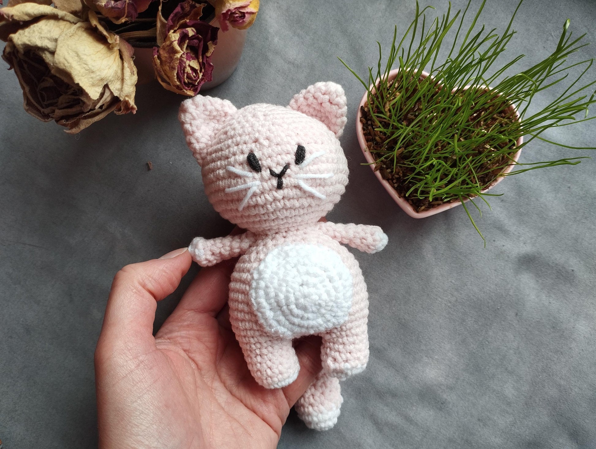 a hand holding a small crocheted cat next to a potted plant