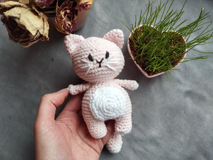 a hand holding a small crocheted cat next to a potted plant