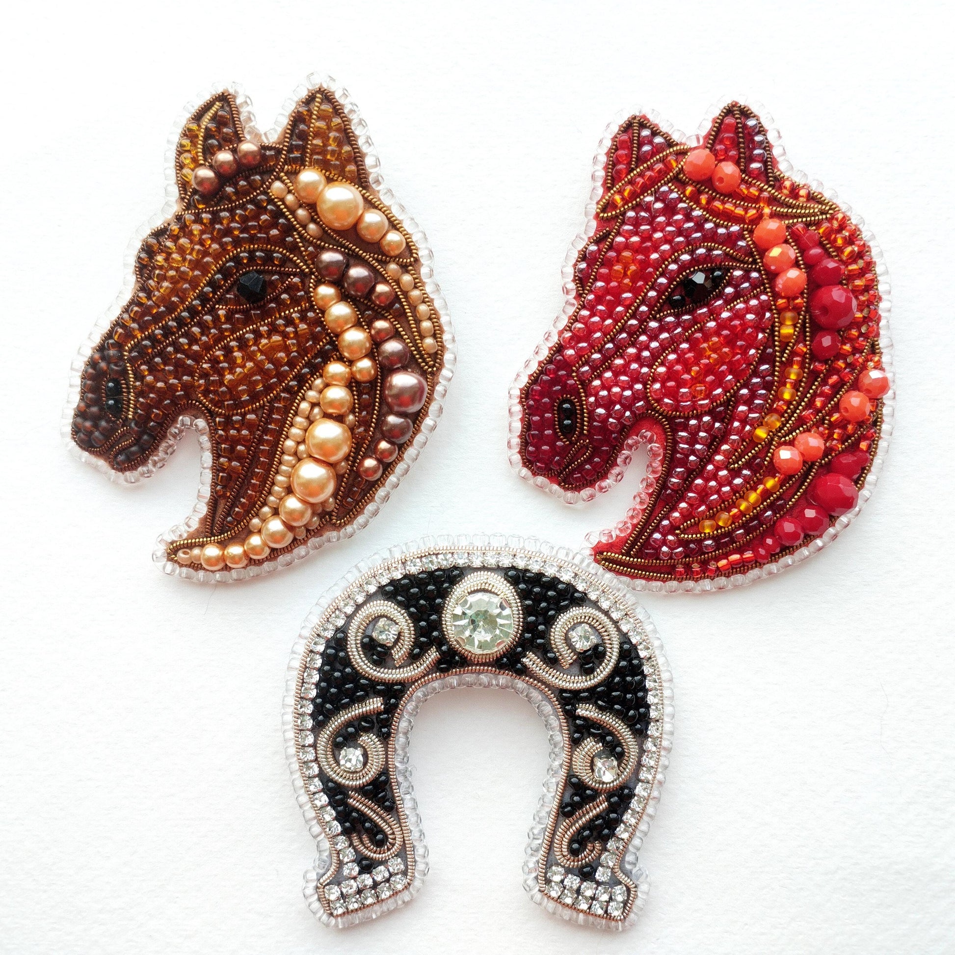 three decorative pieces: two horse head brooches and a horseshoe.