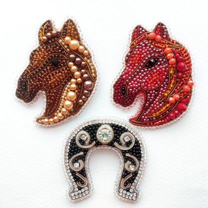 three decorative pieces: two horse head brooches and a horseshoe.