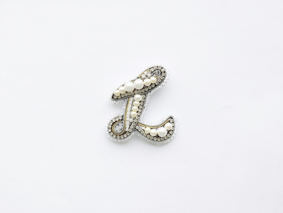 A decorative letter 'L' made of various materials, including pearls and crystals, is shown against a white background.