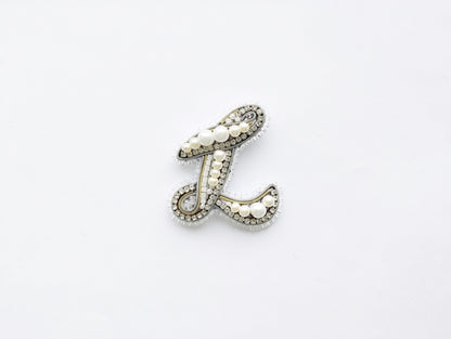 A decorative letter 'L' made of various materials, including pearls and crystals, is shown against a white background.