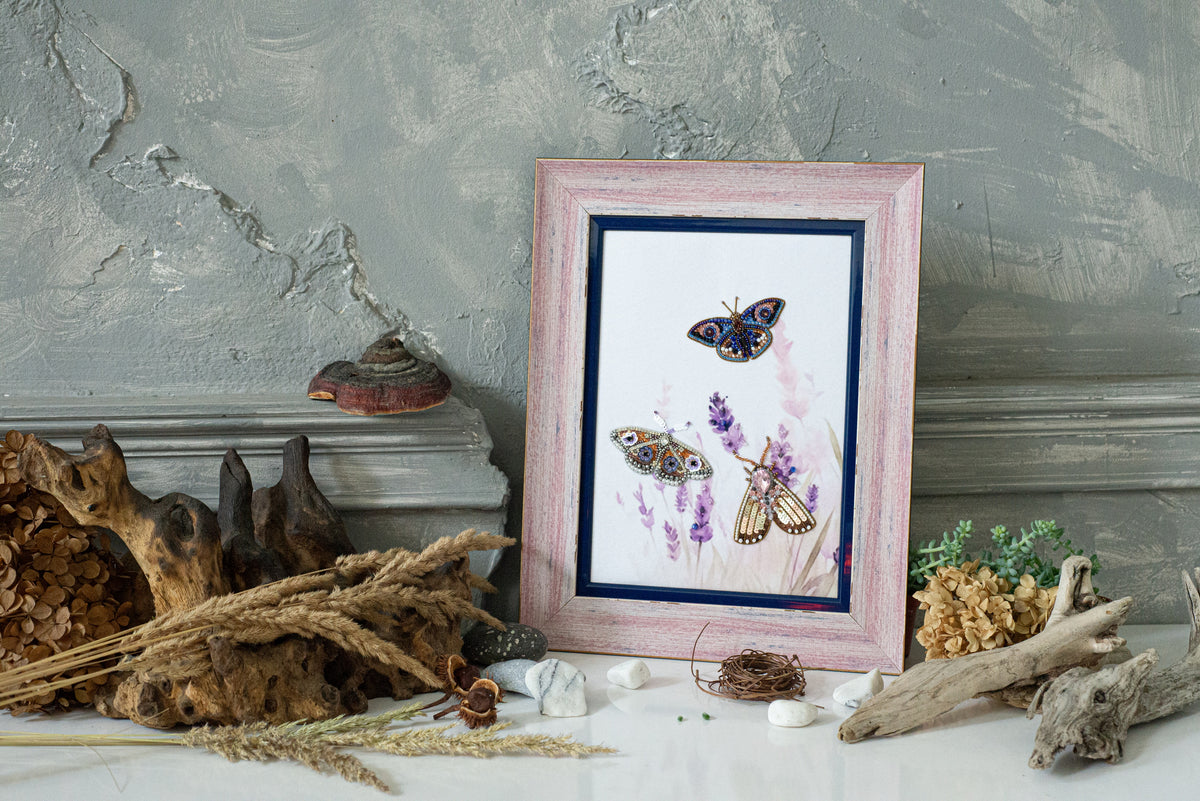 a framed painting of butterflies on a white background, surrounded by various natural elements such as driftwood, dried flowers, and rocks.
