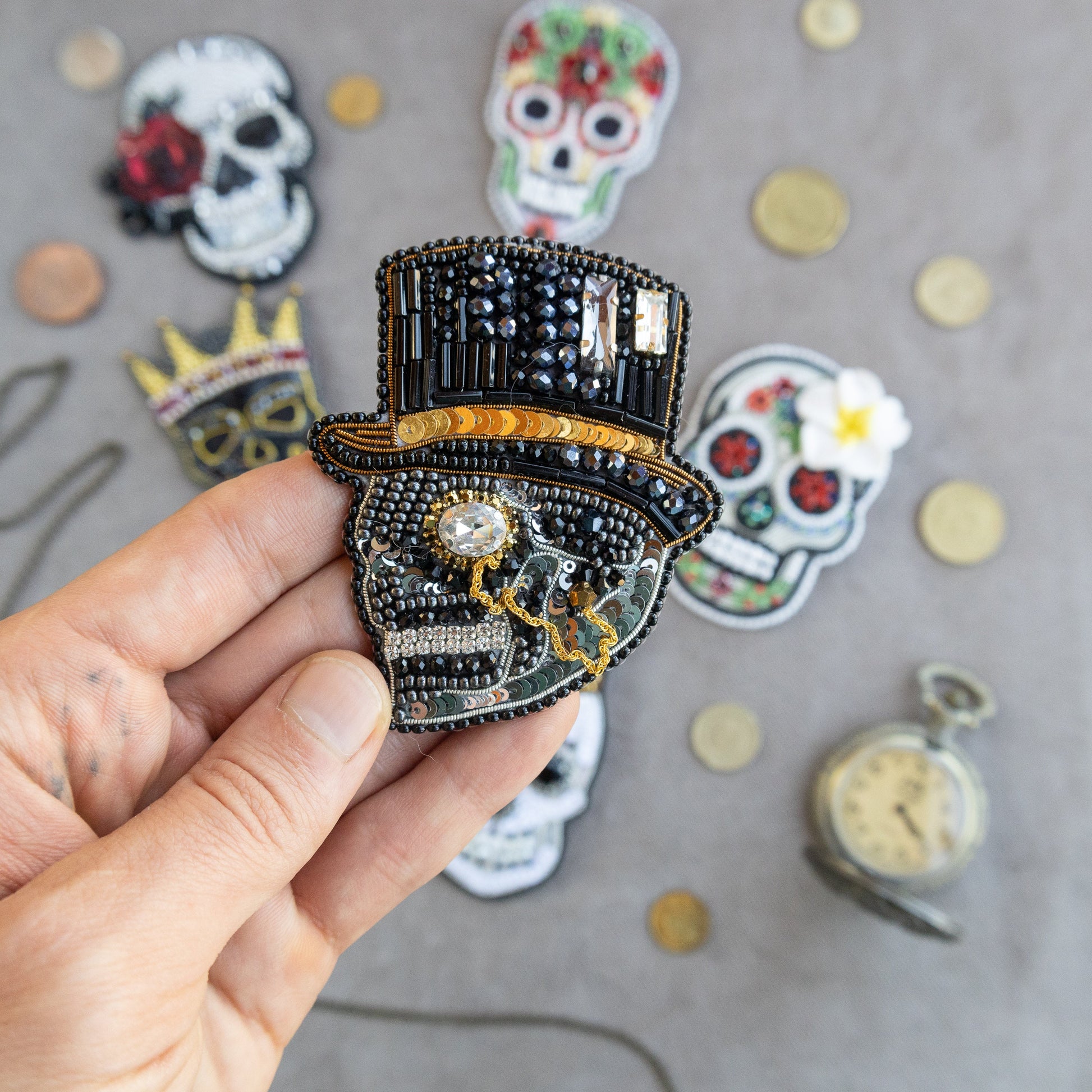 a hand holding a brooch with a clock and skull on it