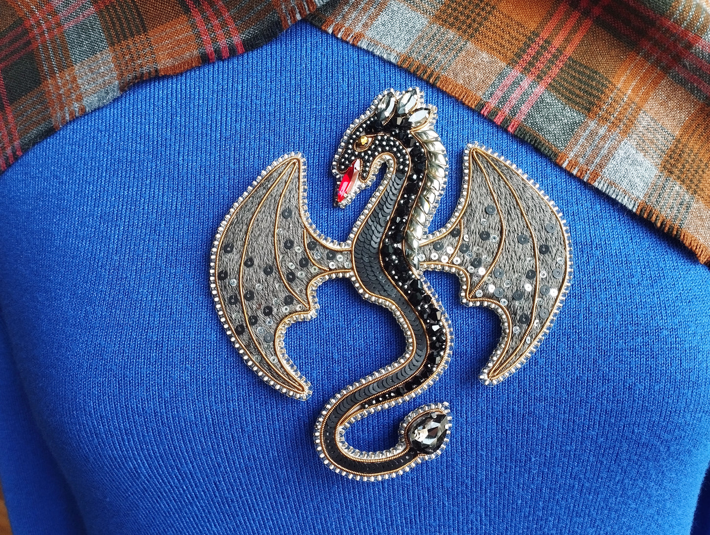 A close-up of a blue sweater with a decorative dragon brooch on it.