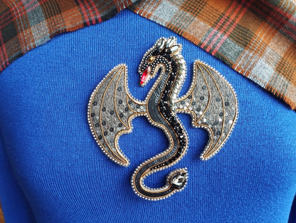 A close-up of a blue sweater with a decorative dragon brooch on it.