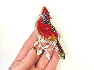 a hand holding a brooch with a bird on it