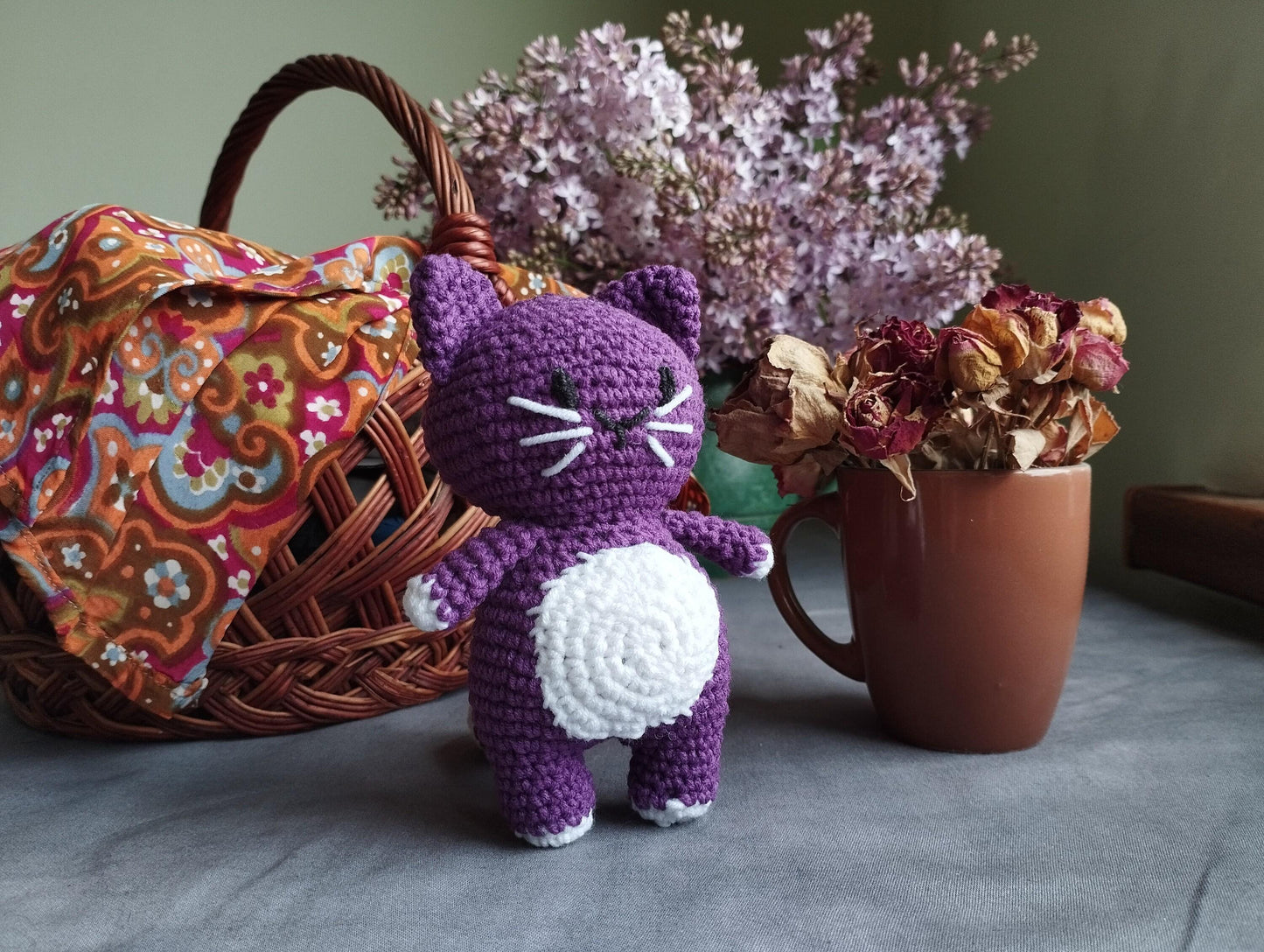 a purple crocheted cat next to a basket of flowers