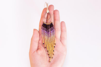 A hand holding a beaded earring with a long, tassel-like design.