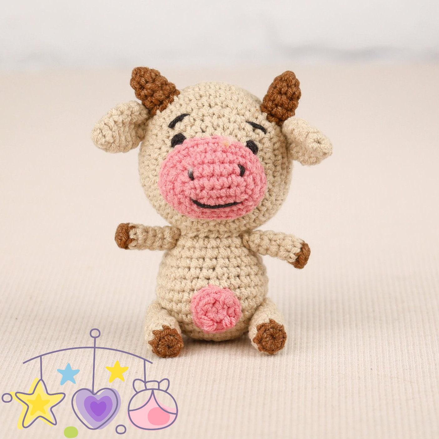 a small toy cow sitting next to a ball of yarn